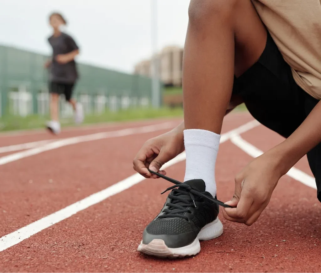 A kid tying his shoe on a running track, representing the opportunities for kids to stay active and engaged through donations to Playground Stars.