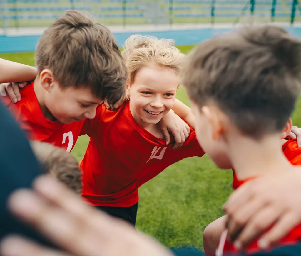 A team of boys with their arms around one another on a field, representing the sense of community and teamwork supported by donations to Playground Stars.