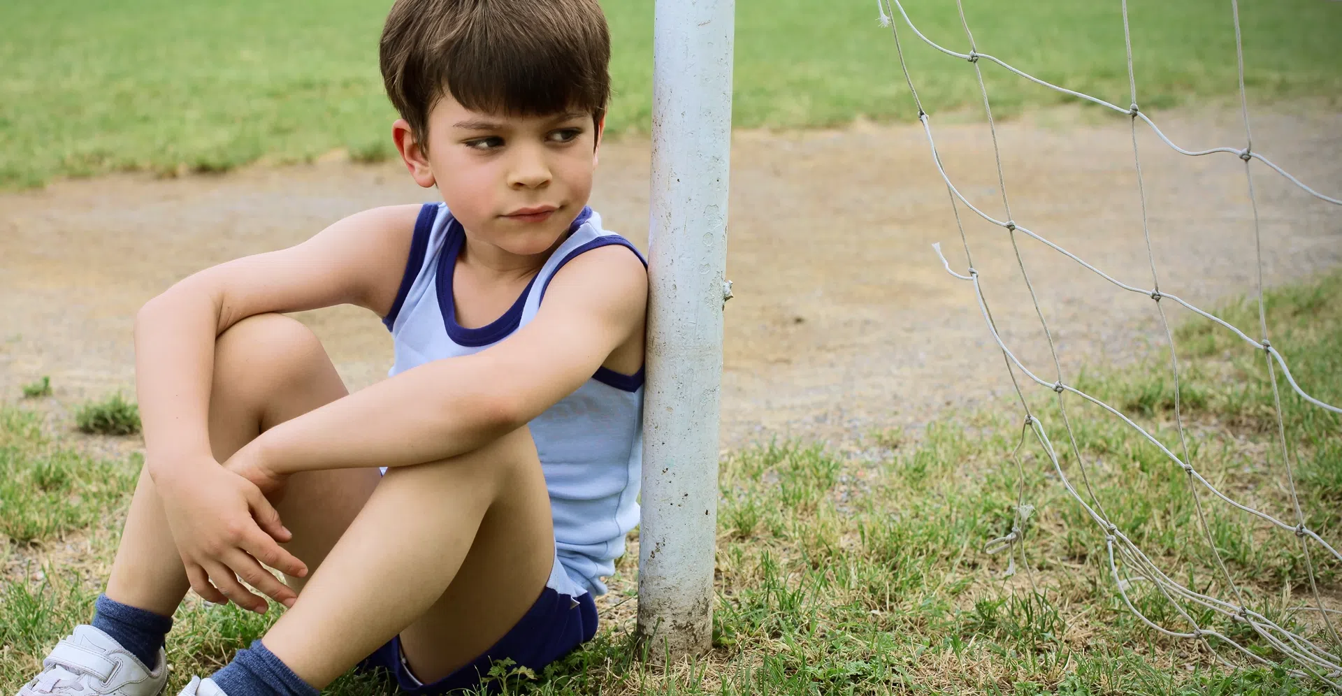 Child sitting alone outside, highlighting the need for accessible youth sports opportunities.