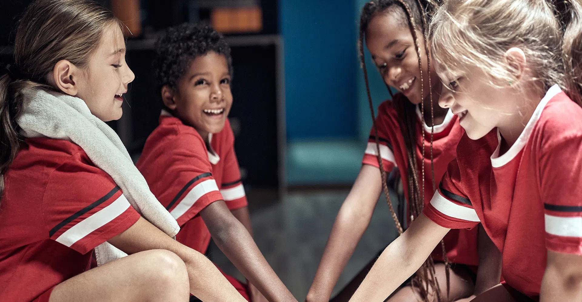 Four kids in red sports shirts putting their hands together, representing the spirit of teamwork in youth sports, made possible by your donation to Playground Stars.