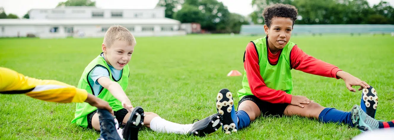 Two young soccer players stretching on a community field, highlighting the importance of local youth sports funding and accessibility.